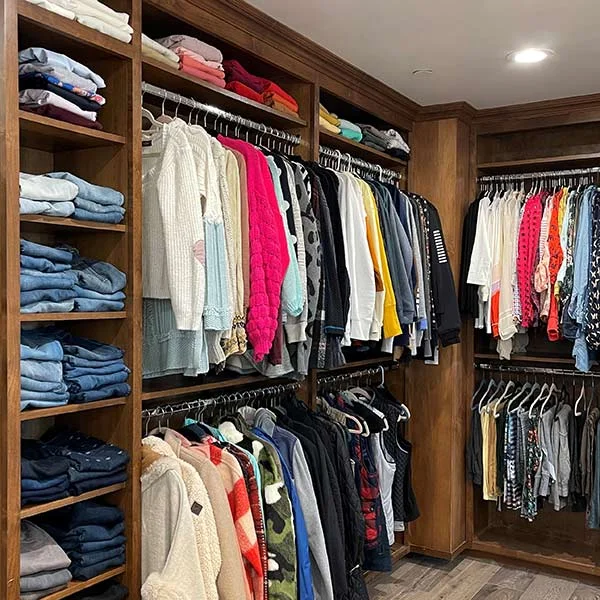 Walk-in closet with folded jeans and sweaters on wood shelves and clothes hung by color